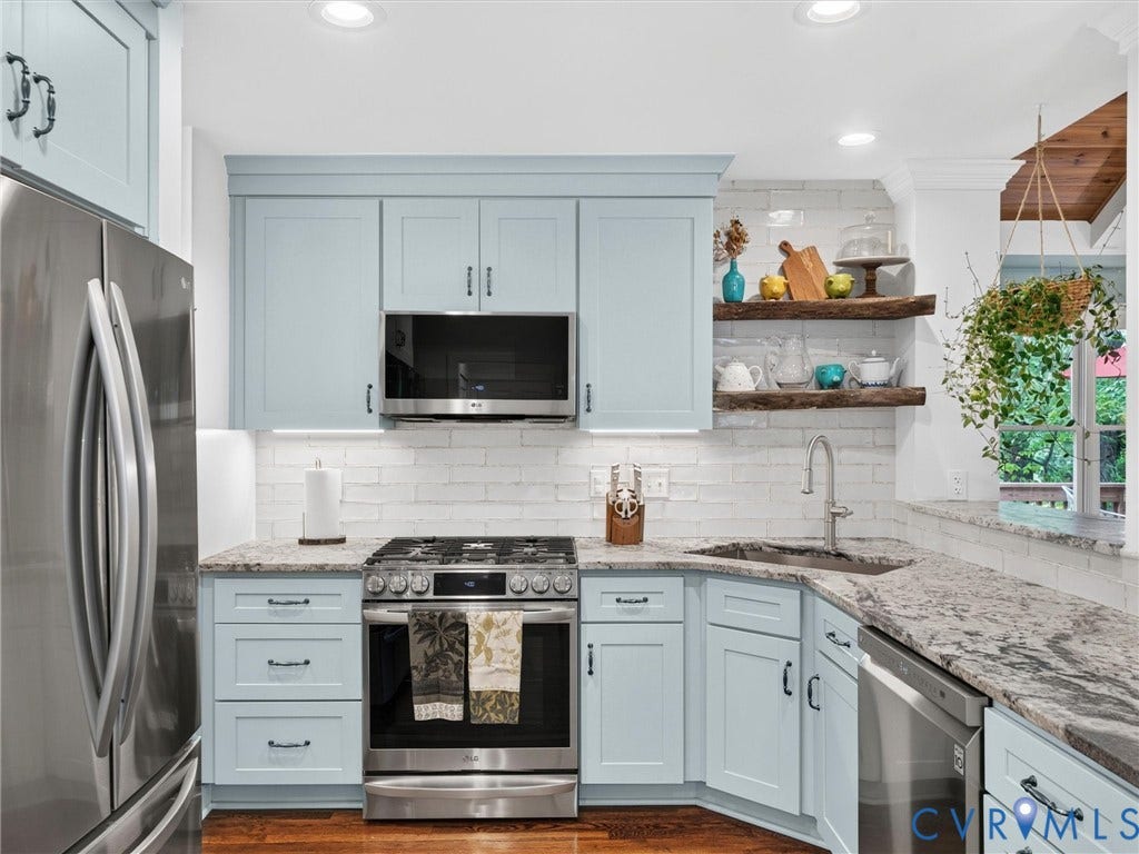 Light blue cabinetry with black hardware, stainless steel appliances, granite countertops, white subway tile backsplash, and wood-finish flooring