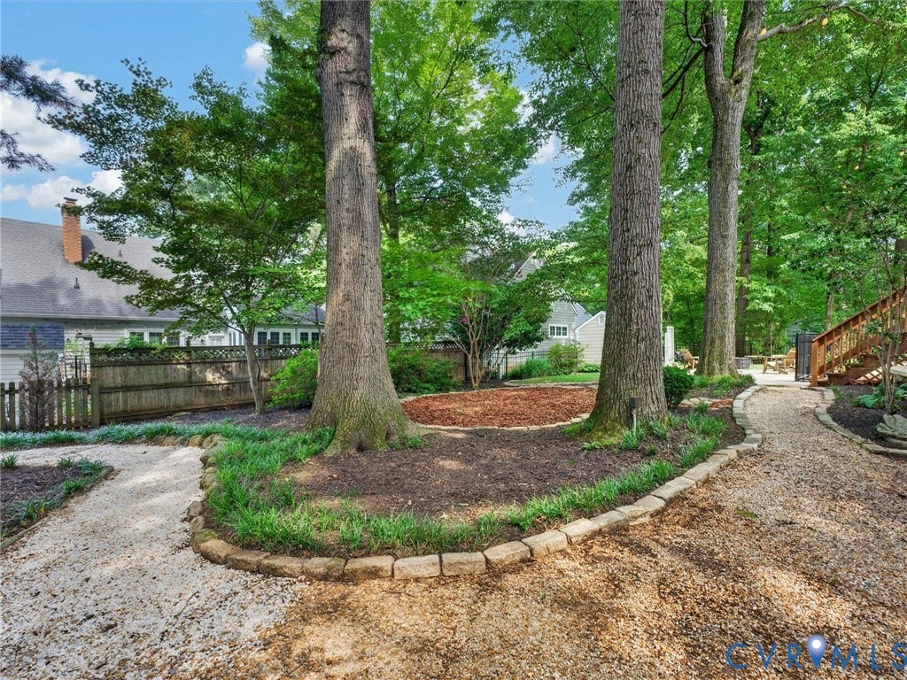 Gravel pathways, stone garden edging, mature trees, wood fencing, and a terraced wood deck