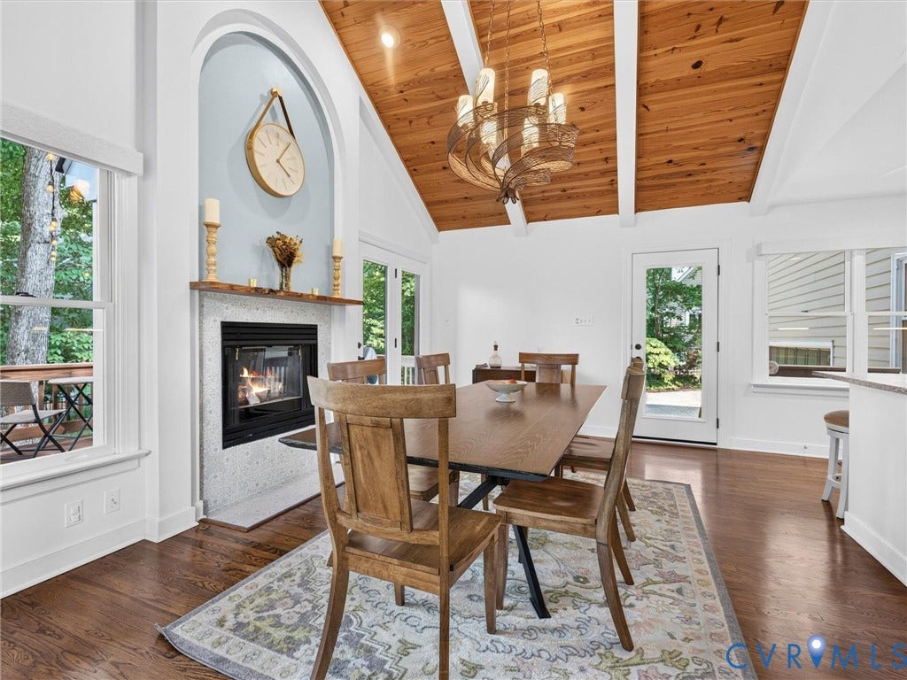 Vaulted wood-paneled ceiling, fireplace with hearth, hardwood flooring, multiple windows, and a glass-paneled door