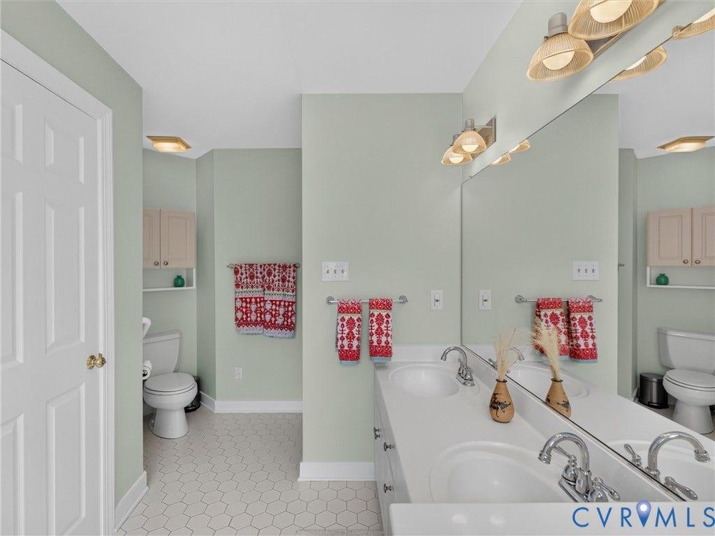 Dual vanity with integrated sinks and chrome fixtures, large wall-mounted mirror, overhead lighting, and hexagonal floor tiling