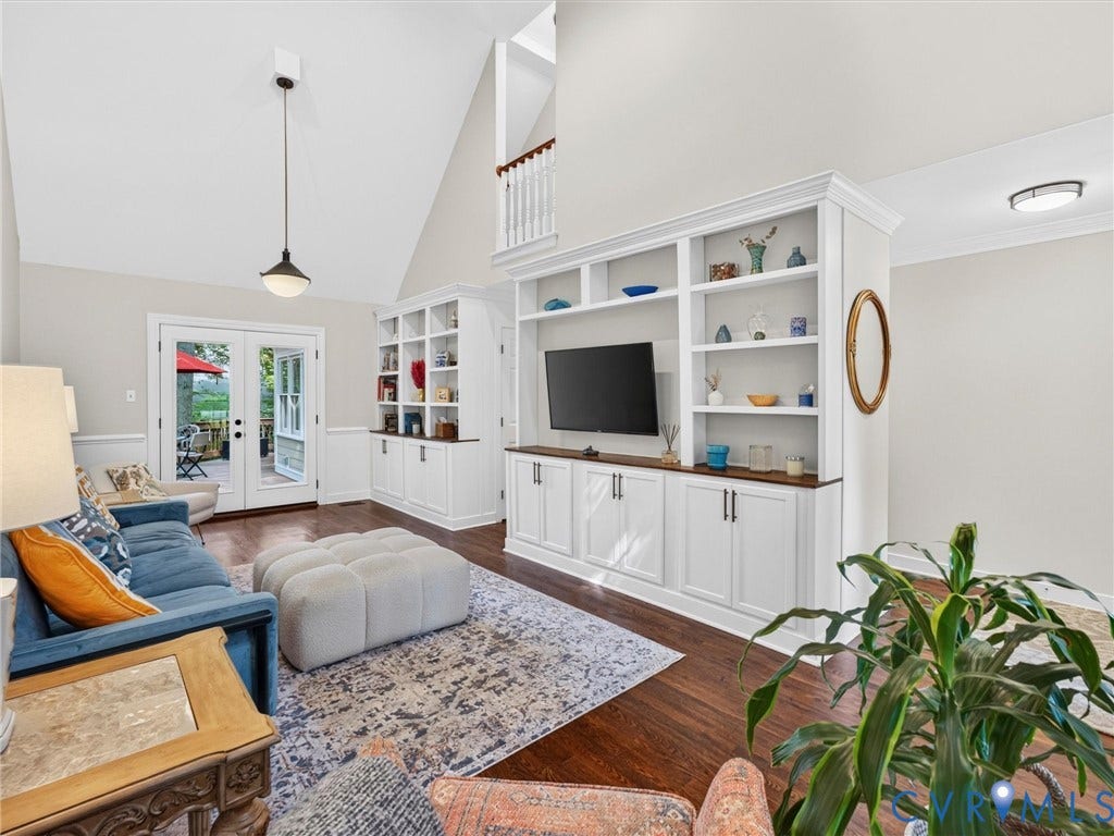Vaulted ceiling, dark wood-finish flooring, white built-in cabinetry, white french doors, and a decorative pendant light