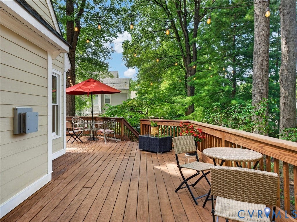 Expansive outdoor wood deck with natural wood railing, string lighting, and mature trees surrounding