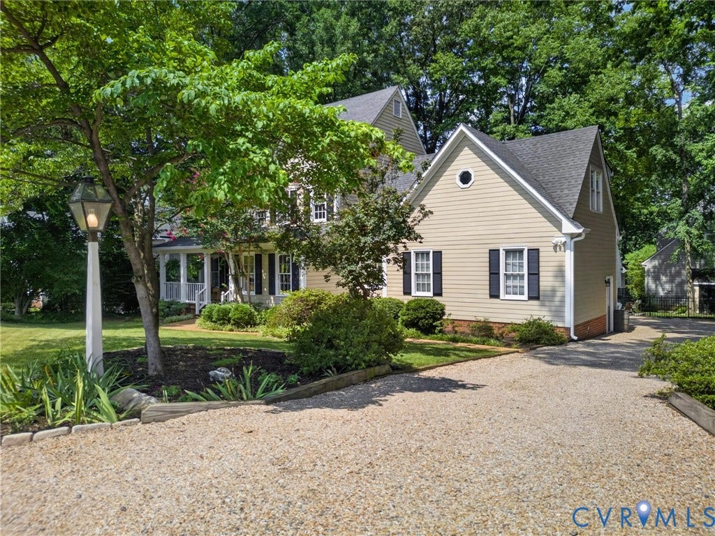 Gravel driveway bordered by manicured landscaping, featuring a porch with white columns and a gable roofline with an oculus window