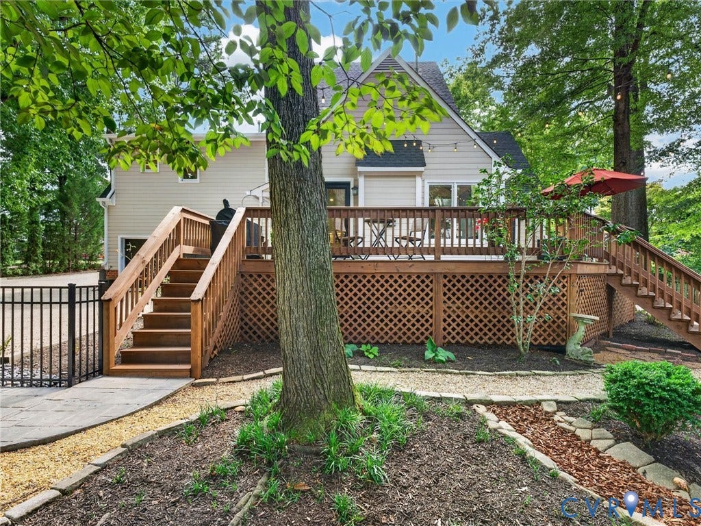 Elevated wood deck with lattice skirting, wood stairs with railings, a stone patio, and a black metal fence