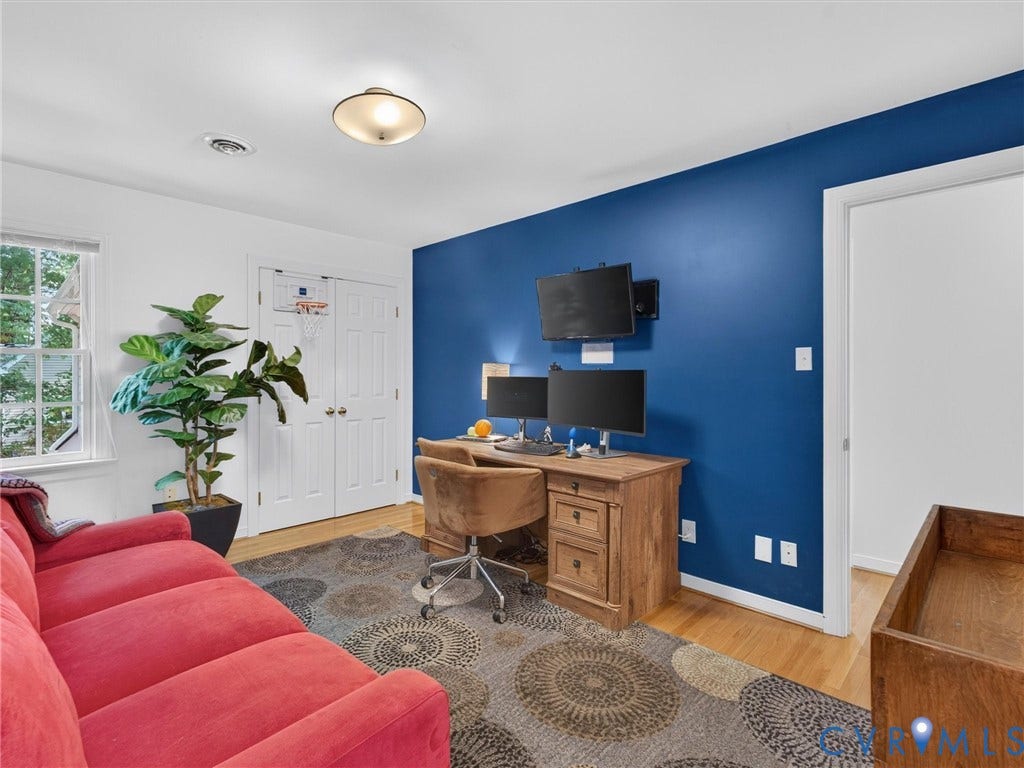 Wood-finish flooring, white double-door closet, window with white trim, wall-mounted light fixture, blue accent wall