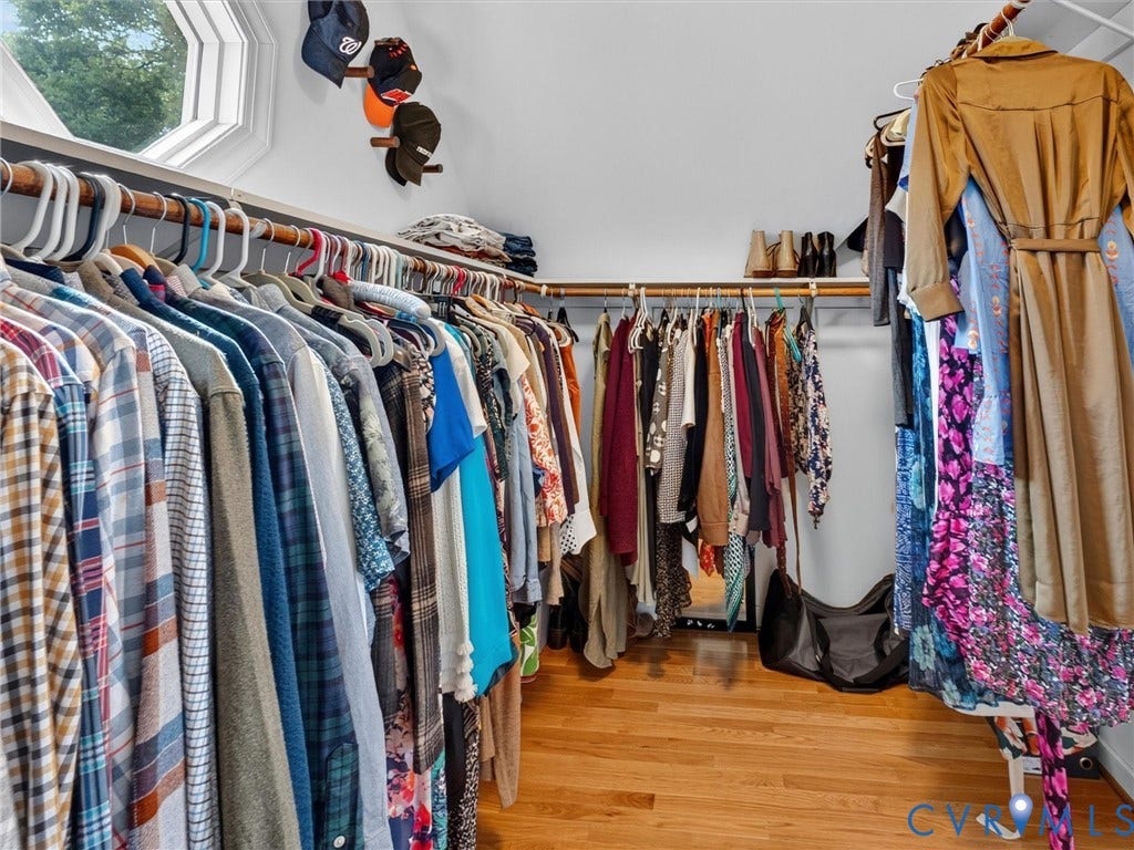 Walk-in closet featuring extensive built-in hanging rods, wood-finish flooring, and a multi-faceted window