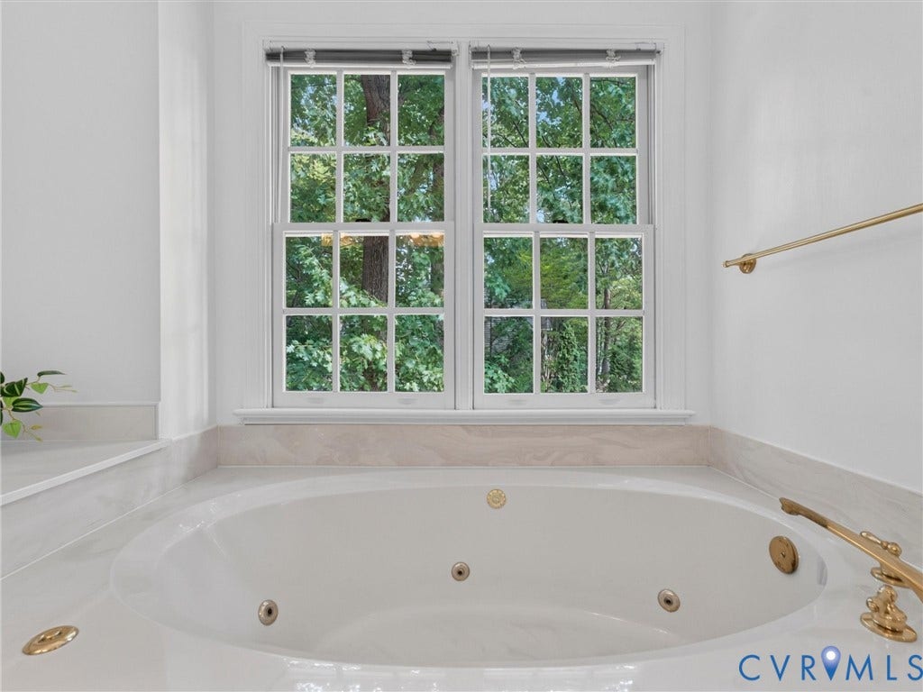 Soaking tub with brass fixtures, surrounded by a light-toned countertop