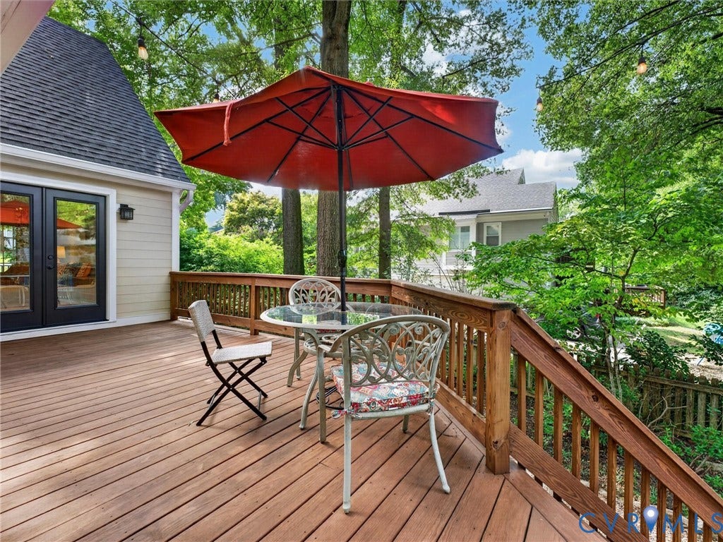 Expansive wood deck with a natural wood railing, directly accessible via black-framed glass double doors, and surrounded by mature trees