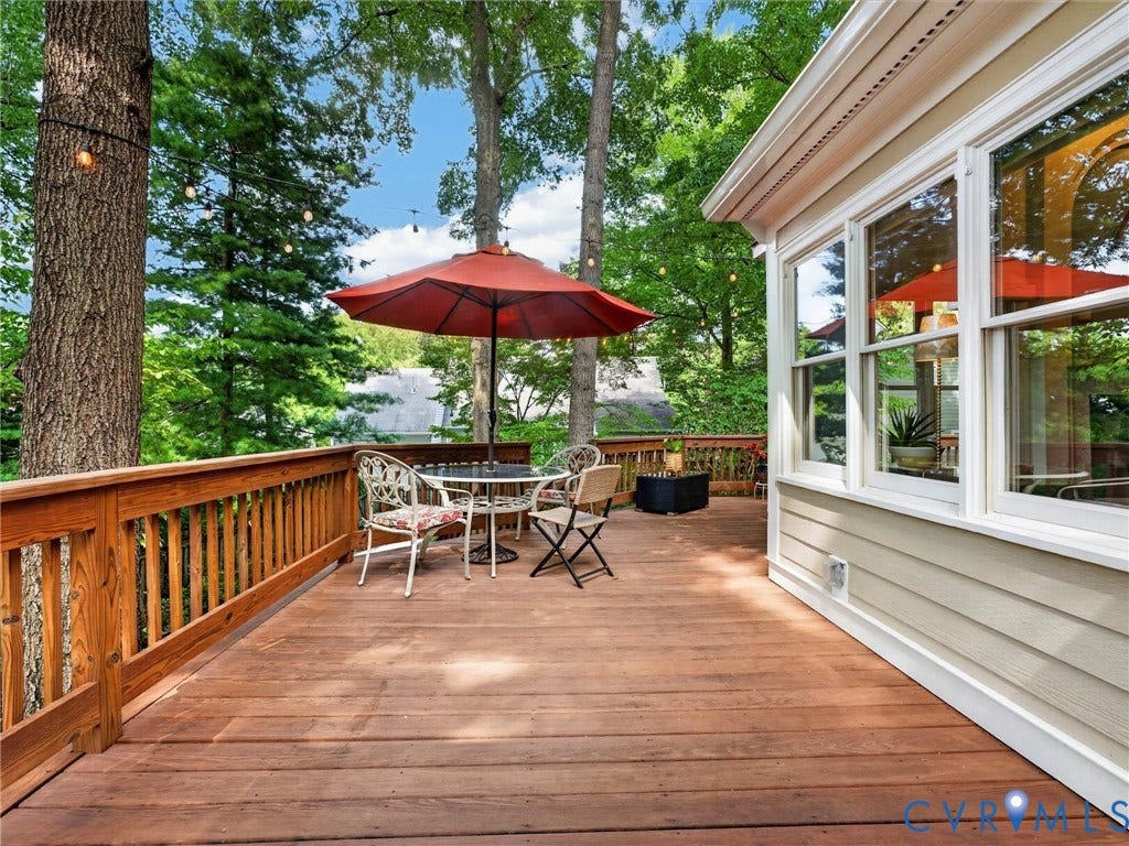 Expansive wood deck with a natural wood railing, light beige siding, and multiple large windows
