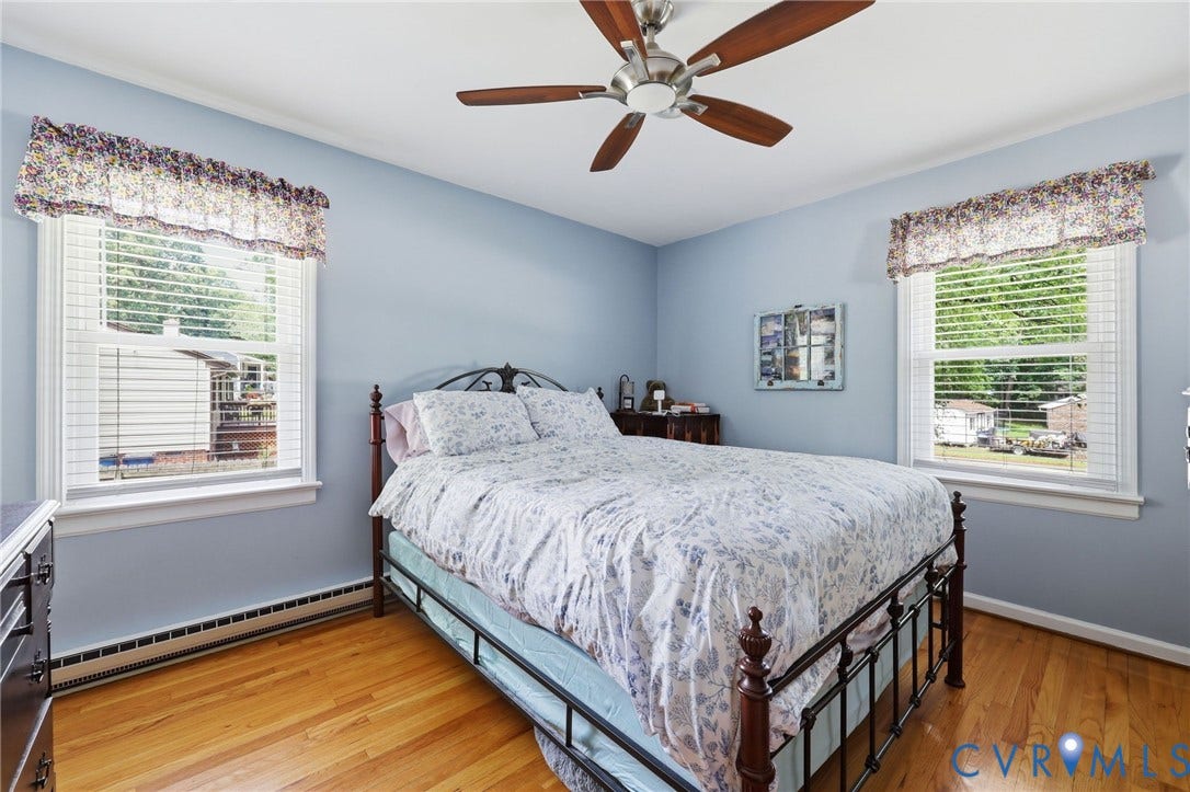 3300 Woodsong Drive, Midlothian, VA 23112 Bright room featuring two windows with horizontal blinds, wood-finish flooring, light blue walls, and a ceiling fan with wood-finish blades