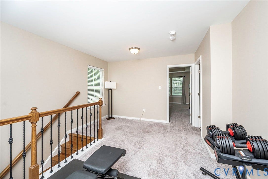 7205 Desert Candle Drive, Moseley, VA 23120 Carpeted upper-level landing with a window featuring blinds, a ceiling-mounted light fixture, and a doorway leading to an interior room