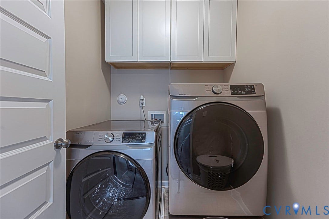 7205 Desert Candle Drive, Moseley, VA 23120 Dedicated laundry space featuring a white paneled door, light gray walls, built-in upper cabinetry, and contemporary washing appliances