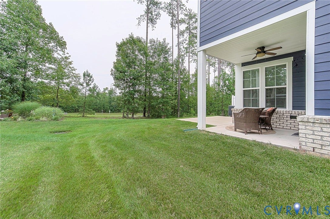 7205 Desert Candle Drive, Moseley, VA 23120 Spacious lawn area with a covered patio featuring a ceiling fan and white brick accents