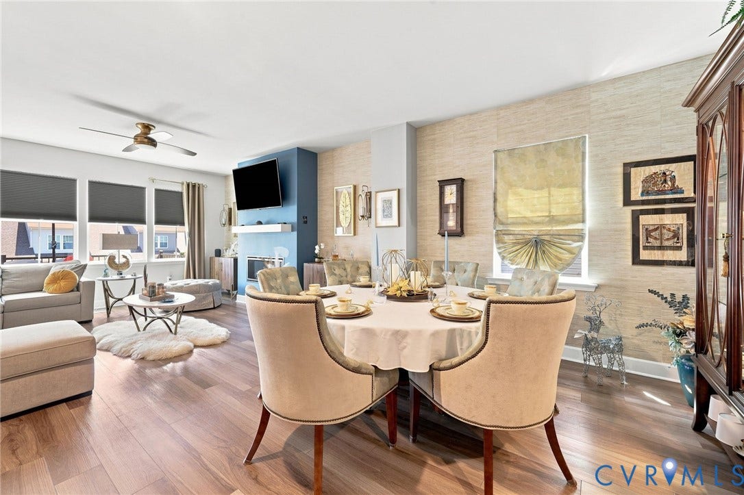 Open-concept living and dining area featuring wood-finish flooring, a contemporary ceiling fan, and multiple windows
