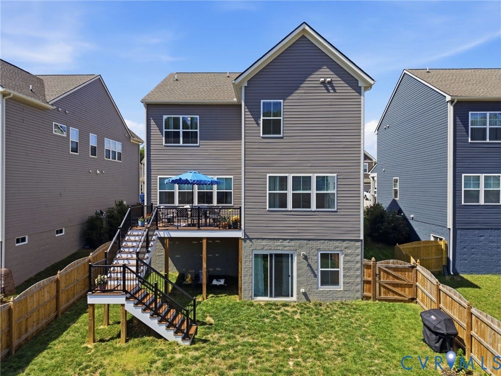 Elevated two-story home featuring a spacious rear yard with mature landscaping, wooden privacy fencing, and a multi-level deck with metal railings