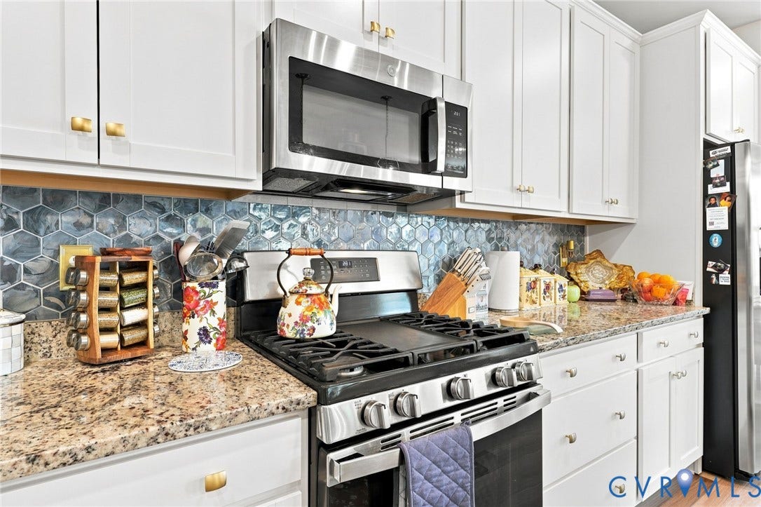 Kitchen featuring white cabinetry with gold-toned hardware, stainless steel appliances, a hexagon tile backsplash, and granite countertops