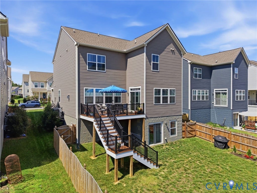 Spacious two-story home featuring gray fiber cement siding, multiple windows with blue accents, and a multi-level deck system