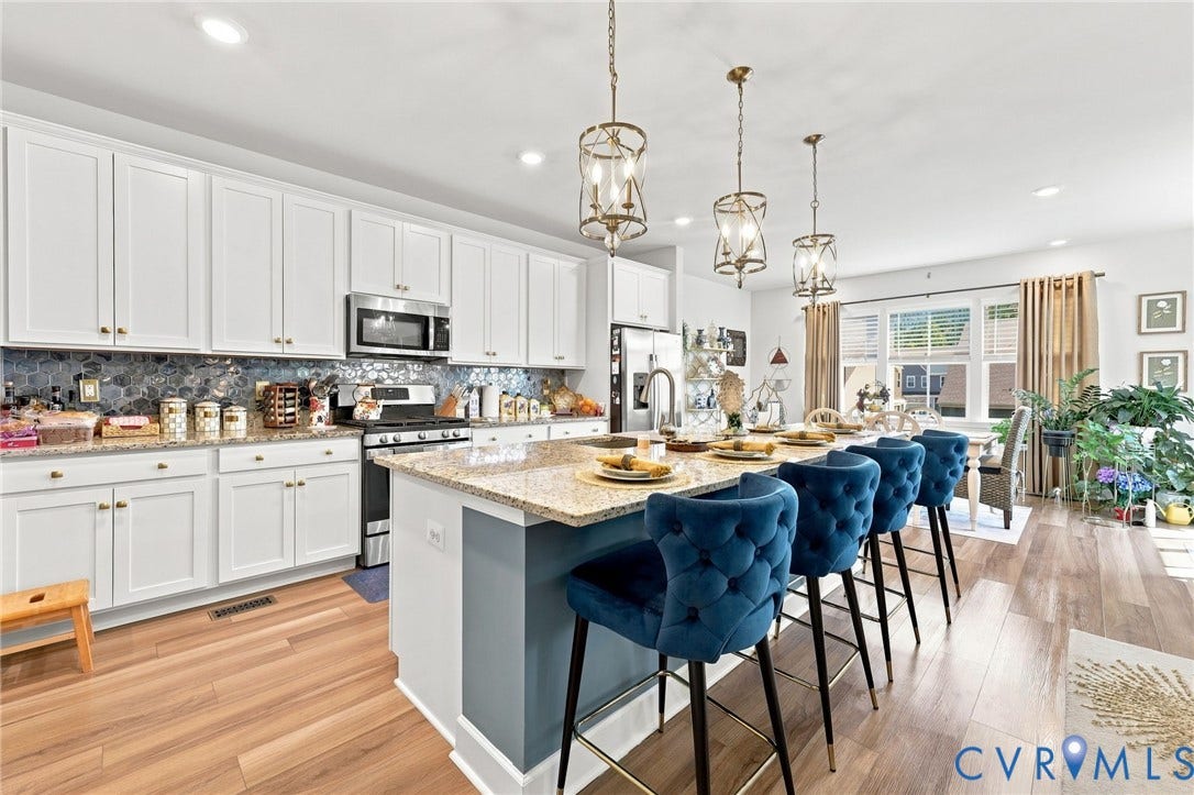 Gourmet kitchen featuring white shaker cabinetry, stainless steel appliances, and a quartz-topped island with seating for three