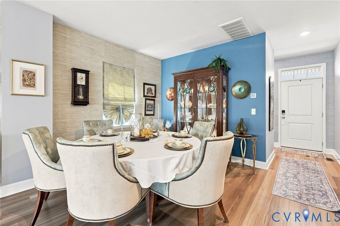 Dining area featuring wood-finish flooring, a wall with textured wall covering, and a window with a Roman shade