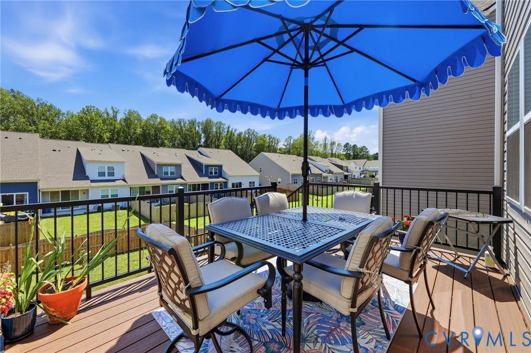 Expansive composite deck featuring a dining table with seating for four, integrated black metal railing, and a blue scalloped patio umbrella providing shade
