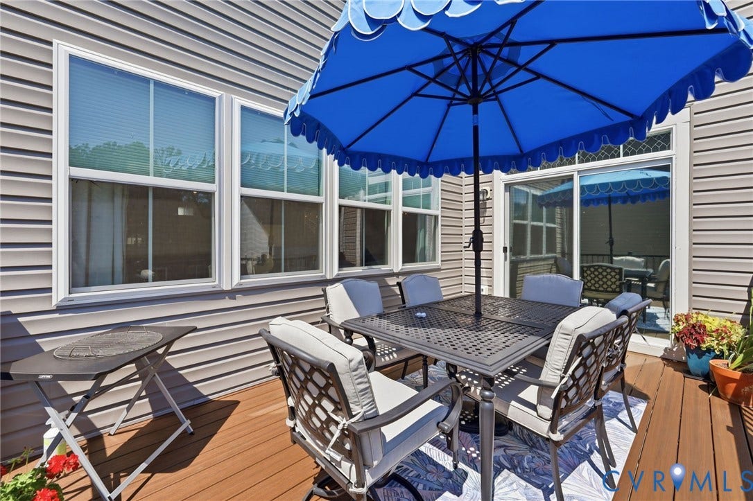 Spacious composite deck featuring a wood-finish surface, dining table with seating for four, cushioned lounge chairs, and a large blue umbrella with scalloped edging