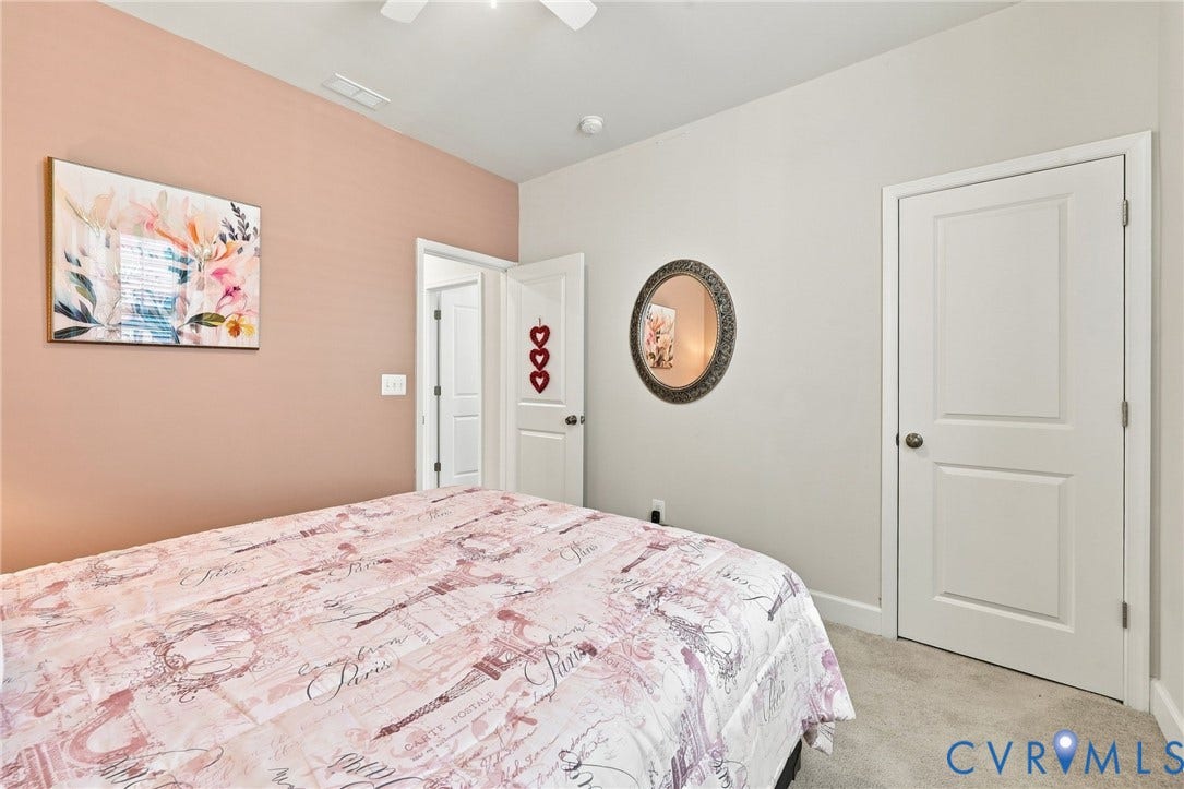 Spacious bedroom with a two-panel interior door, plush carpet flooring, and a ceiling fan
