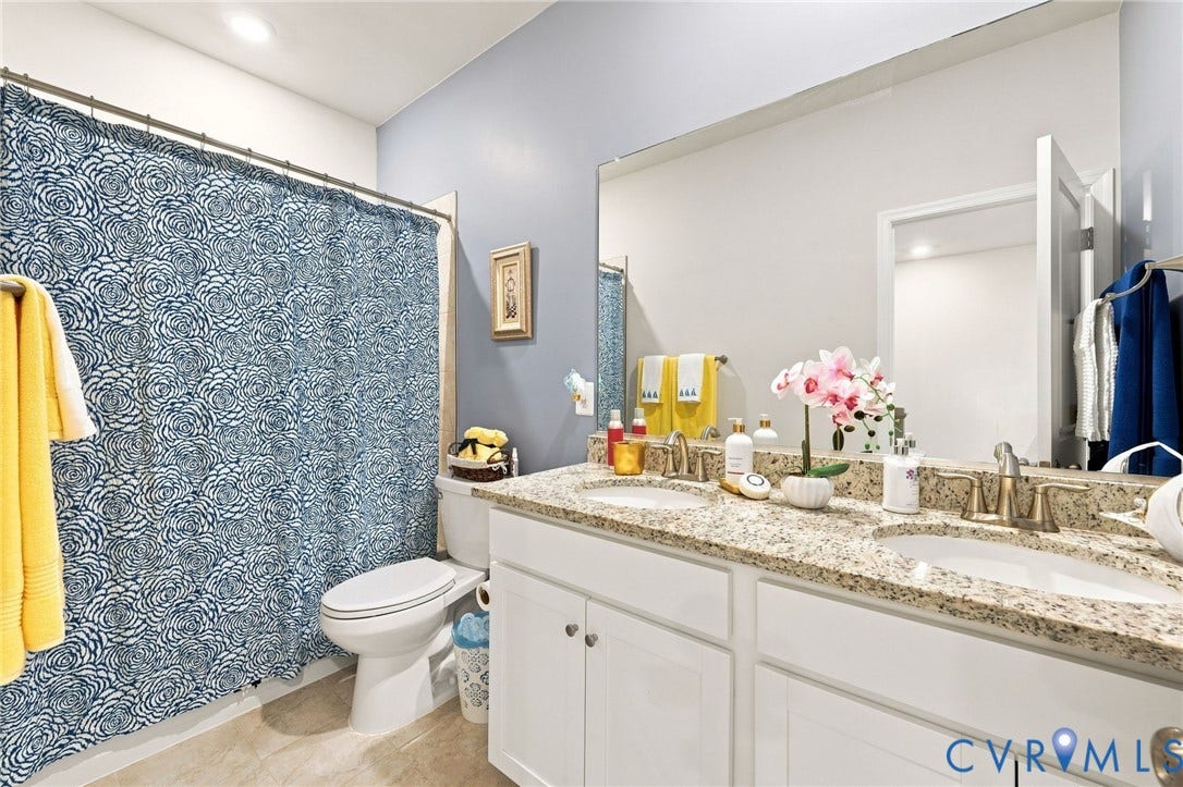 Bathroom featuring a dual vanity with a granite countertop, undermount sinks, and white cabinetry