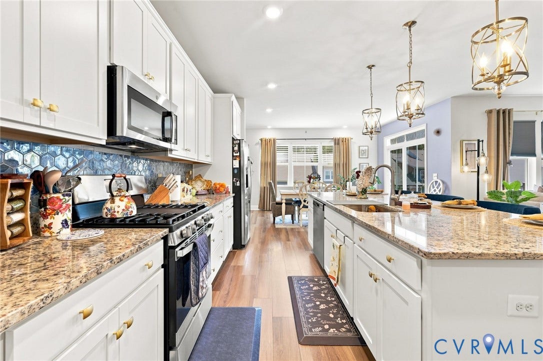 Gourmet kitchen featuring white cabinetry, stainless steel appliances, granite countertops, a mosaic tile backsplash, and a central island with pendant lighting