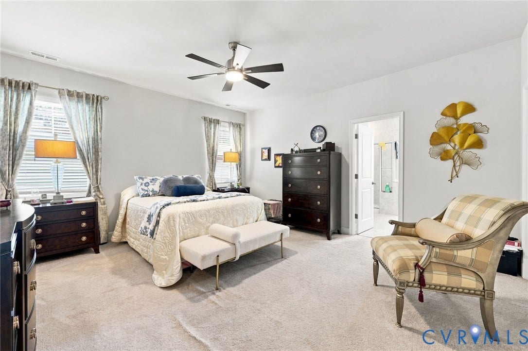 Spacious room featuring light gray walls, carpet flooring, a ceiling fan with integrated lighting, and two windows with blinds