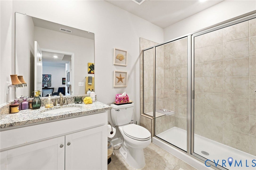 Bathroom featuring a glass-enclosed shower with tile surround, a built-in shower bench, a single vanity with a granite-style countertop, and tile flooring
