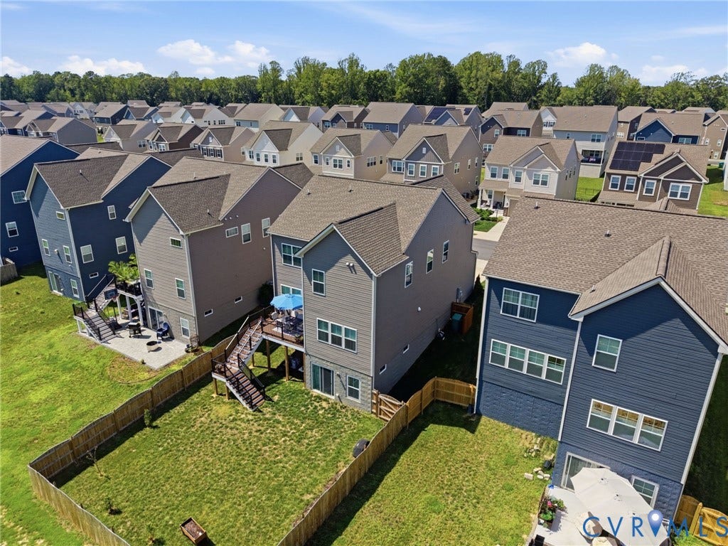 Modern two-story home with contemporary siding and architectural detailing, featuring a spacious fenced backyard with mature landscaping, professional hardscaping, and a multi-car garage with paneled doors