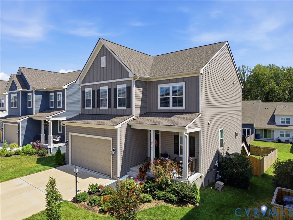 Two-story colonial featuring a taupe and charcoal exterior with architectural gable detailing, two-car attached garage with paneled door, and manicured front landscaping