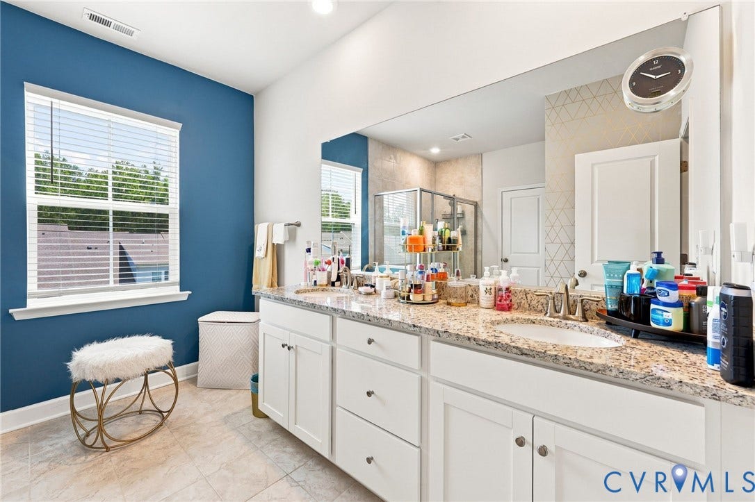 Spa-inspired primary bathroom featuring a double vanity with granite countertop, white cabinetry with ample storage, and polished nickel hardware