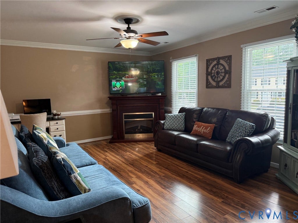 Living area featuring wood-finish flooring, a ceiling fan with light fixture, and crown molding