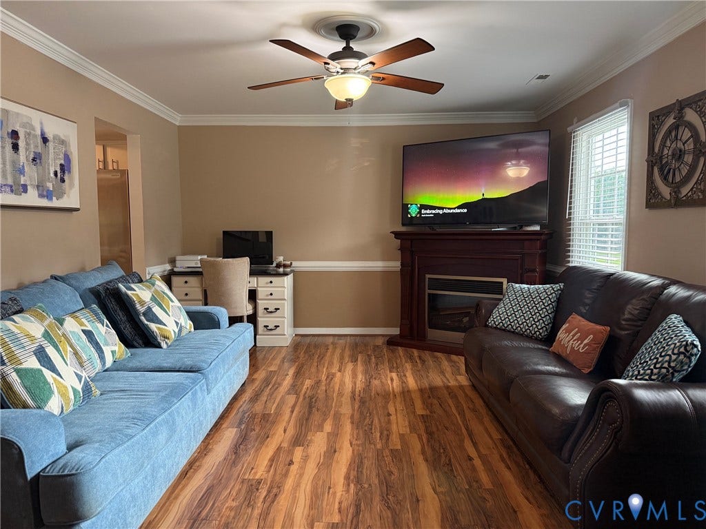 Living area featuring wood-finish flooring, a decorative fireplace with a wood mantel, and crown molding