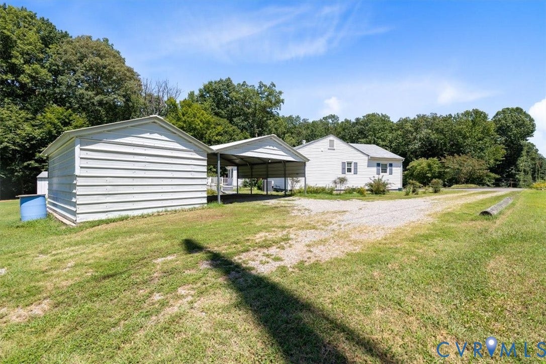 2311 Georges Road, Powhatan, VA 23139 White siding residence featuring a gravel driveway, mature trees, a detached metal outbuilding, and an attached metal carport structure