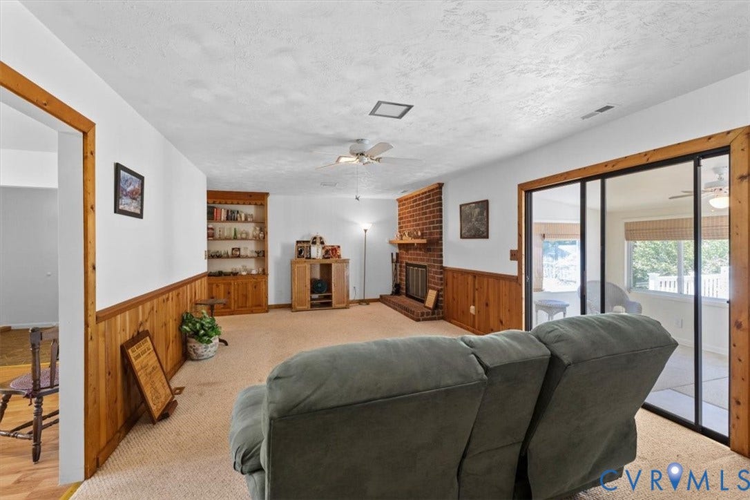 2311 Georges Road, Powhatan, VA 23139 Living area featuring carpet flooring, brick fireplace with wood mantel, wood paneling, built-in wooden shelving, and sliding glass doors with wood trim
