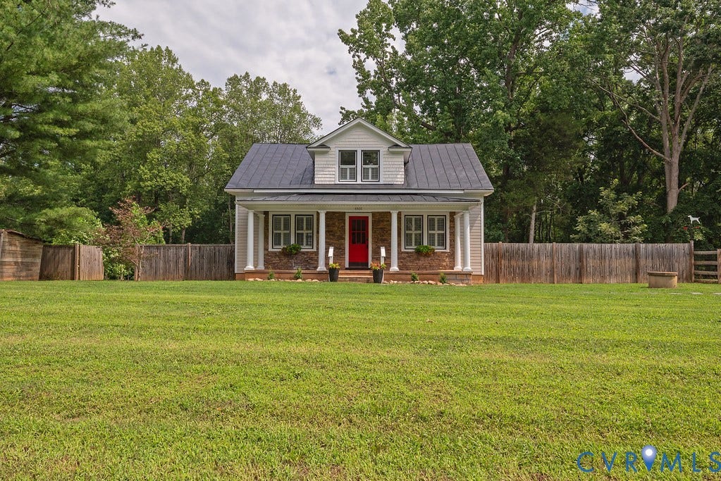 4808 River Road W Road, Goochland, VA 23063 White siding exterior featuring a red entry door, a covered front porch with white columns, a dark shingled roof, and a mature tree line backdrop