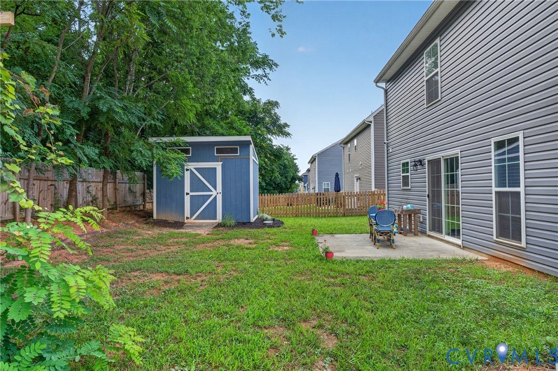 311 Cardinal Road, Countryside, Louisa, VA 23093 Expansive backyard featuring a concrete patio, a blue-painted storage shed with white trim, and a full privacy fence