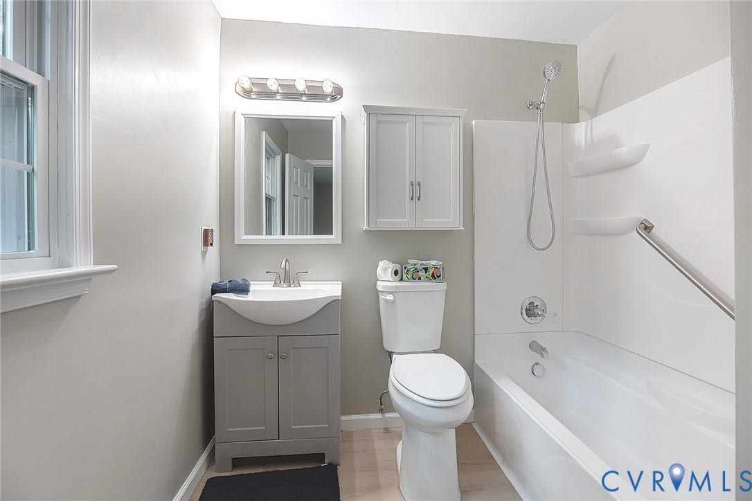 14001 Branched Antler Drive, Antler Ridge, Midlothian, VA 23112 Light wood-finish flooring, white window trim, vanity with integrated basin, mirrored medicine cabinet, and a white bathtub with shower head