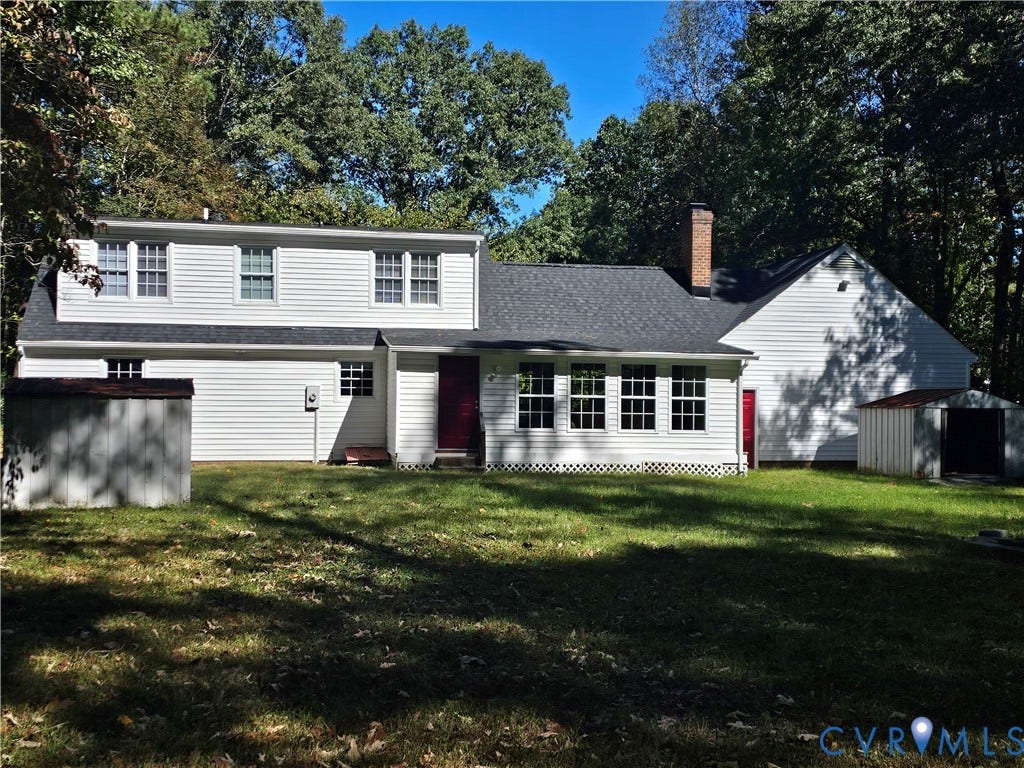12870 King William Road, King William, VA 23086 Exterior siding featuring white horizontal lap, a dark asphalt shingle roof, a brick chimney, and grid-pattern window panes, set on a wooded lot