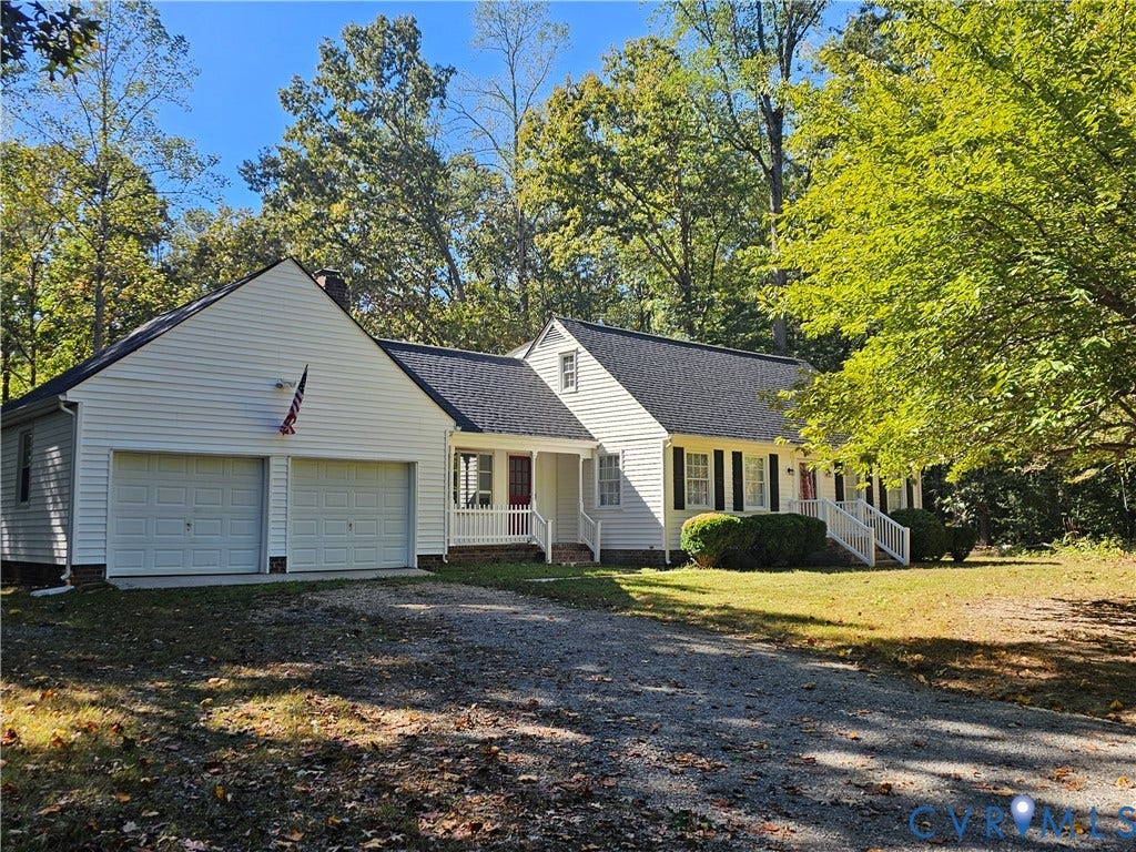 12870 King William Road, King William, VA 23086 Cape Cod-style residence featuring white siding, dark shutters, a two-car garage, and white railed porch entries, situated on a wooded lot