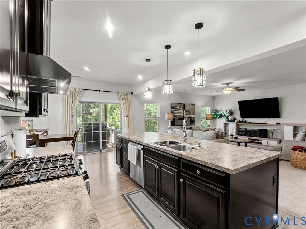 10419 Centralia Station Road, Chester, VA 23831 Kitchen featuring a large island with an integrated sink, dark cabinetry, light-toned countertops, and three decorative pendant lights