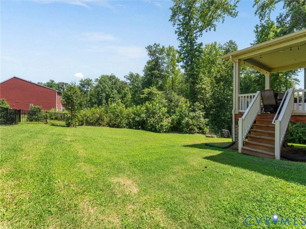 10419 Centralia Station Road, Chester, VA 23831 Expansive rear yard featuring a covered porch with white railings, wood-finish stairs, and a black wrought iron fence bordering mature landscaping