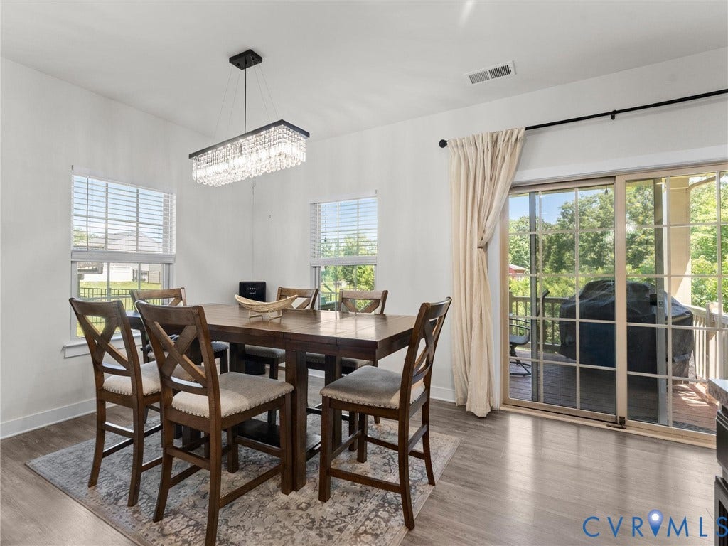 10419 Centralia Station Road, Chester, VA 23831 Bright dining space featuring a rectangular crystal chandelier, two windows with blinds, wood-finish flooring, and a sliding glass door leading to an outdoor deck