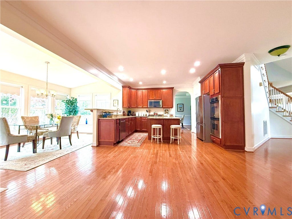 3267 Bayberry Lane, Goochland, VA 23063 Open-concept kitchen and dining area featuring warm wood-finish flooring, rich wood cabinetry, stainless steel appliances, and a central kitchen island with breakfast bar seating