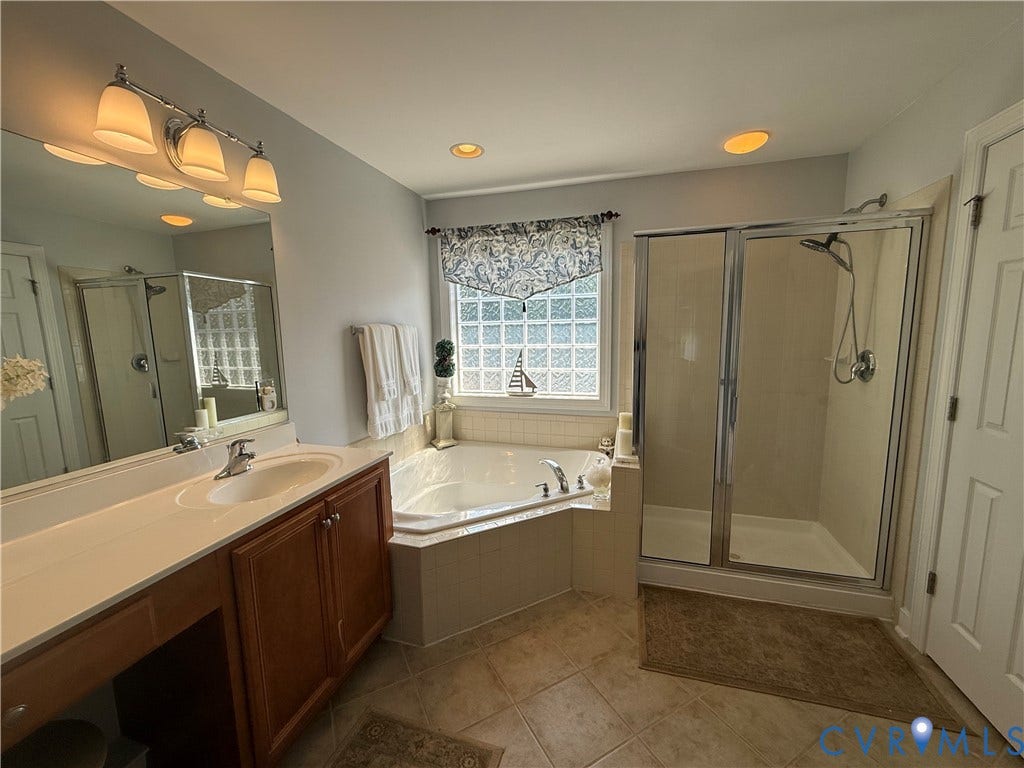 3267 Bayberry Lane, Goochland, VA 23063 Bathroom featuring a double vanity with light wood cabinetry, an integrated soaking tub, a glass-enclosed shower, and a privacy glass block window
