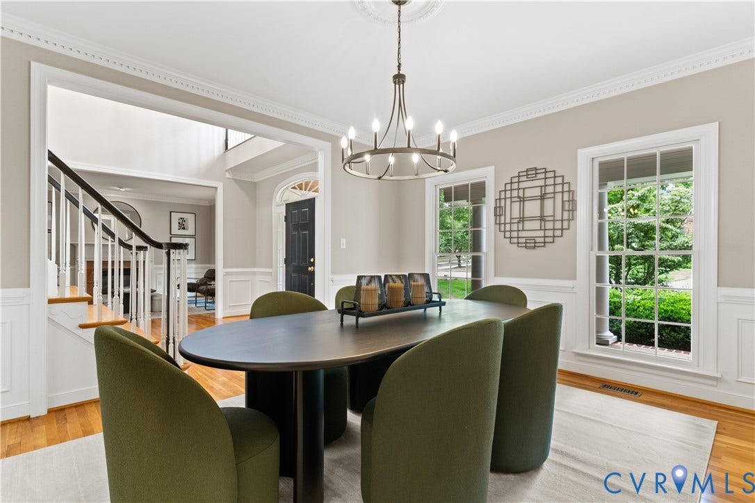 Dining area featuring hardwood flooring, wainscoting, crown molding, and two large windows with exterior greenery visible
