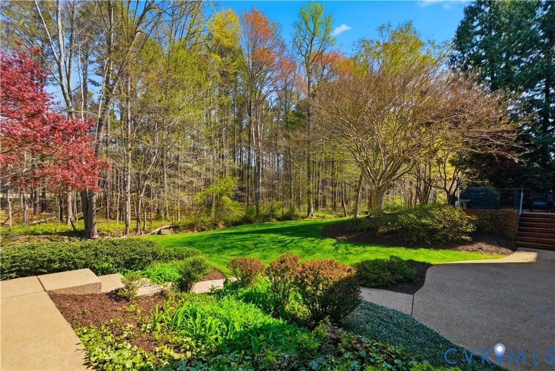 Expansive backyard featuring a manicured lawn, tiered landscaping, mature trees, and a concrete patio with brick steps