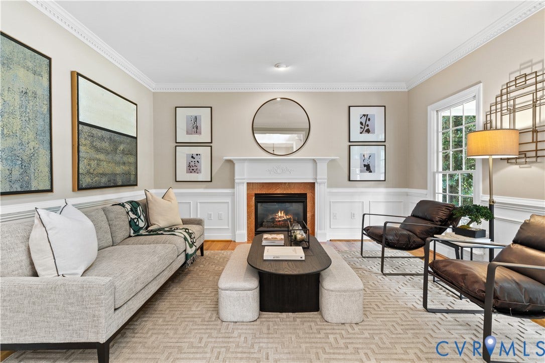 Living area featuring a fireplace with a white mantel, hardwood flooring, crown molding, wainscoting, and floor to ceiling windows